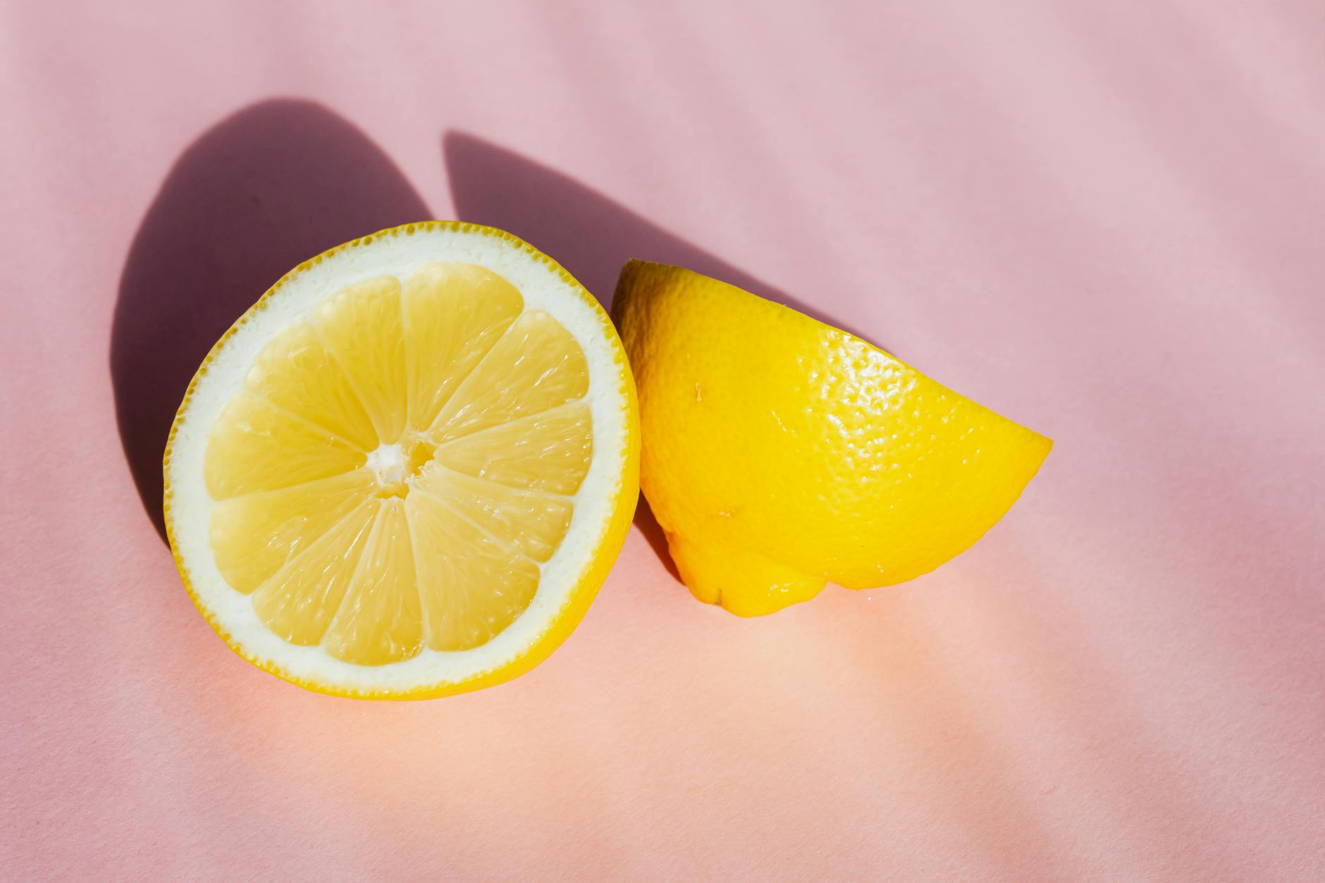 Halves of fresh lemon on pink background in bright light